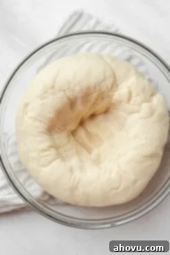 An overhead view of bread dough that's been punched down in a glass mixing bowl.