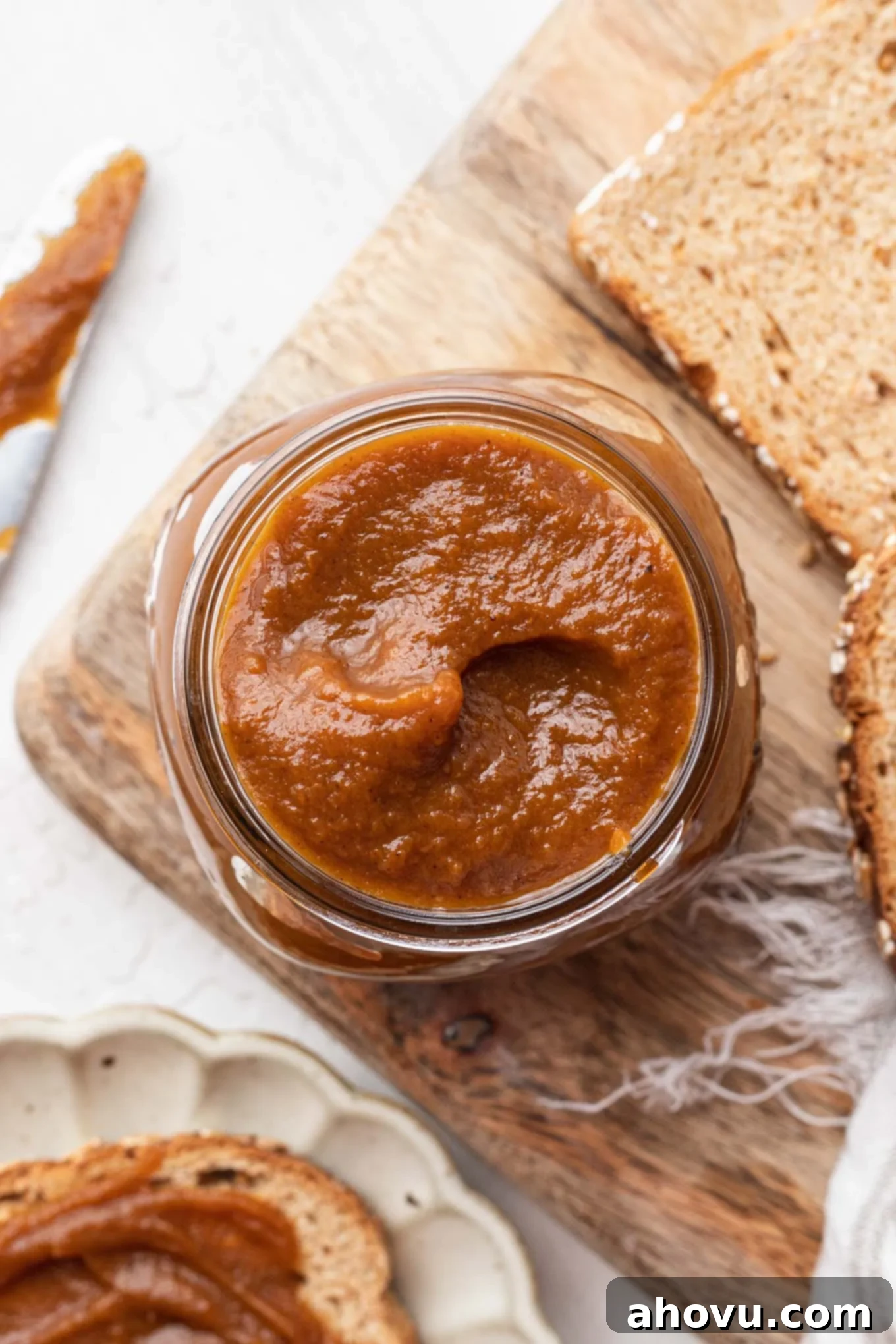 Autumn's Golden Spread 4 A stunning overhead shot featuring a rustic mason jar filled with luscious homemade pumpkin butter, presented on a wooden board alongside inviting slices of bread, ready for a delicious spread.