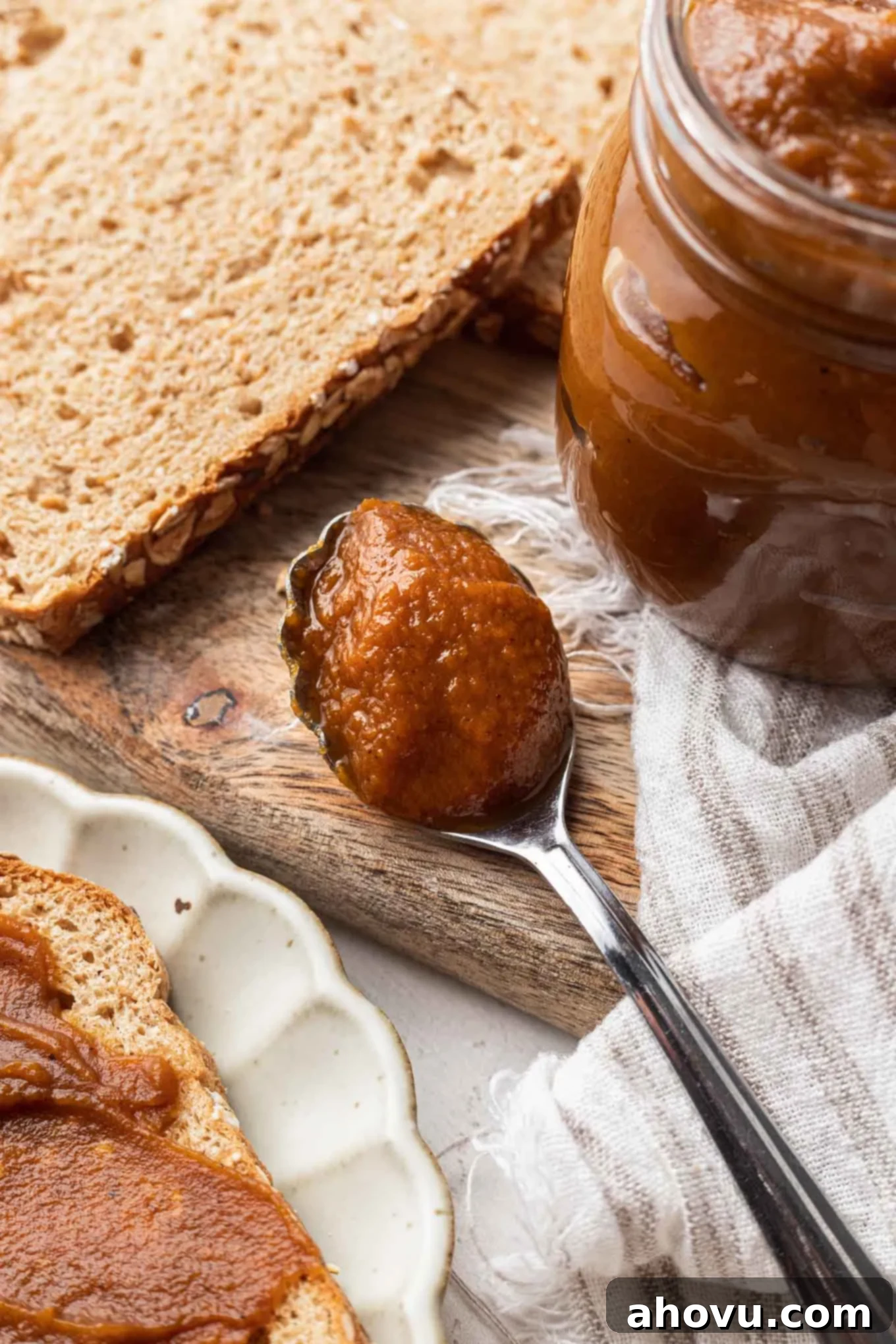 Autumn's Golden Spread 6 A close-up shot of a spoon brimming with rich pumpkin butter, positioned artfully next to a full jar and slices of bread on a wooden surface.