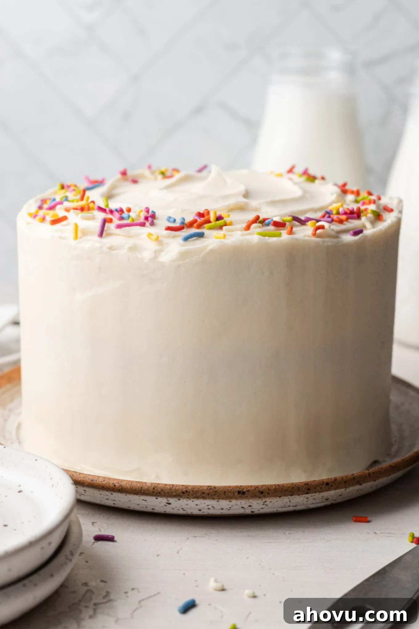 A beautifully frosted 6-inch vanilla cake on a speckled white plate, ready to be served.