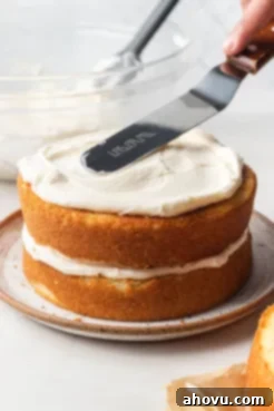 A 6-inch vanilla cake being expertly assembled and frosted on a plate, showcasing the layers.