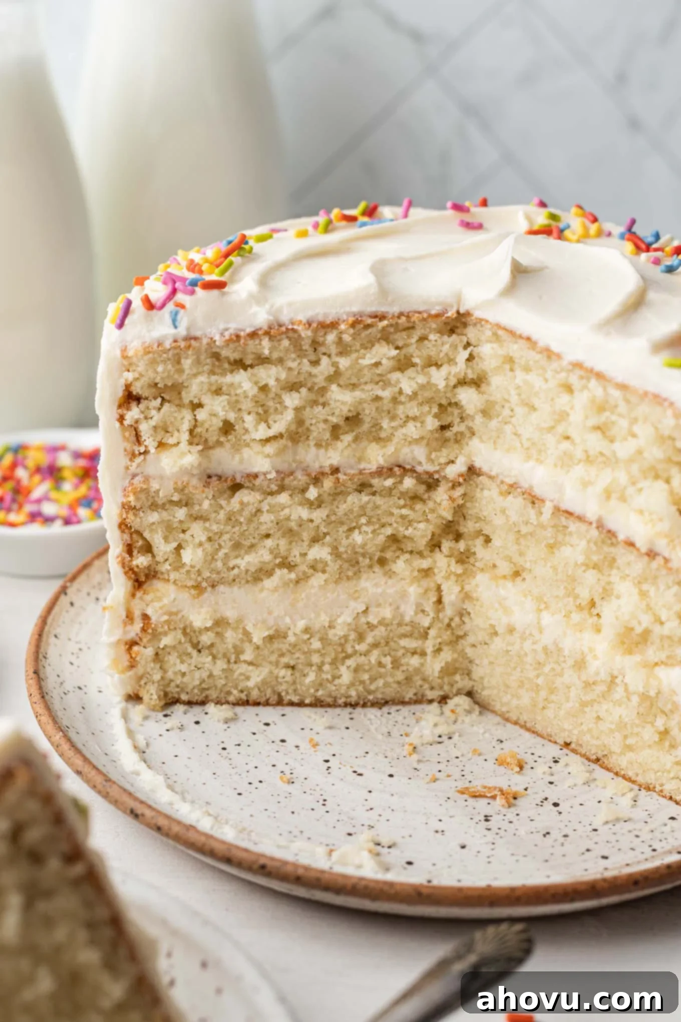 A charming side view of a small vanilla cake, with sections elegantly cut out to display its perfectly baked layers and frosting.