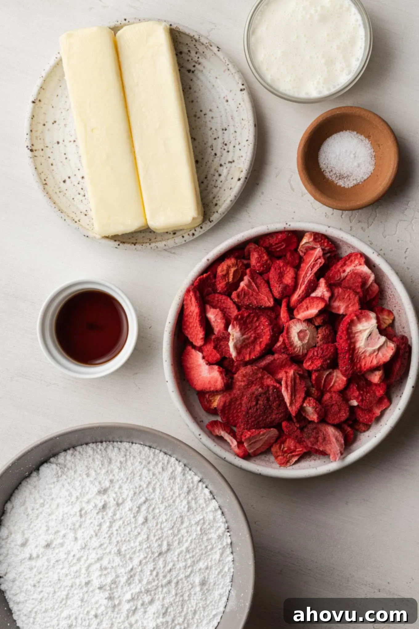 An overhead view showcasing the simple ingredients required for homemade strawberry buttercream: freeze-dried strawberries, butter, powdered sugar, heavy cream, and vanilla extract.