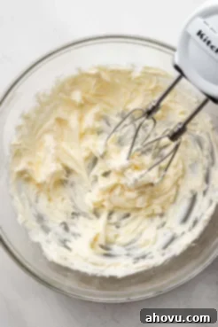 Creamed, softened unsalted butter in a clear glass mixing bowl, being whipped smooth by a hand mixer.