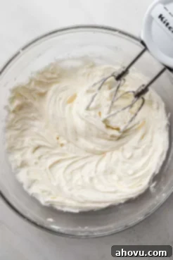 Softened butter and powdered sugar being creamed together in a glass mixing bowl with a hand mixer, creating a smooth base for the frosting.