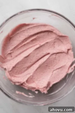 A vibrant pink strawberry buttercream frosting, perfectly mixed and swirled in a clear glass mixing bowl.