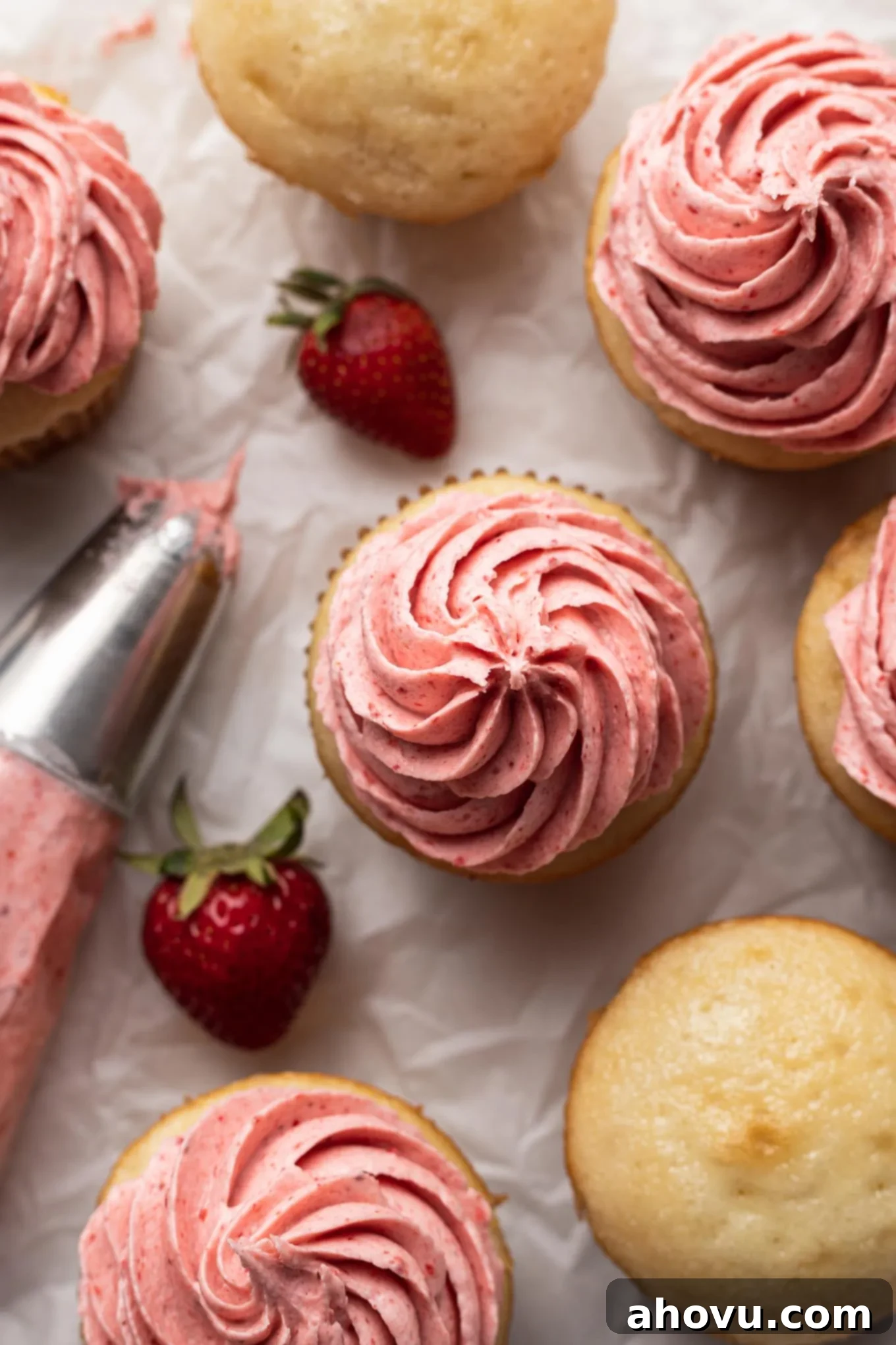 An inviting overhead view of strawberry frosted cupcakes, scattered fresh berries, and a piping bag resting, signaling a delicious baking adventure.