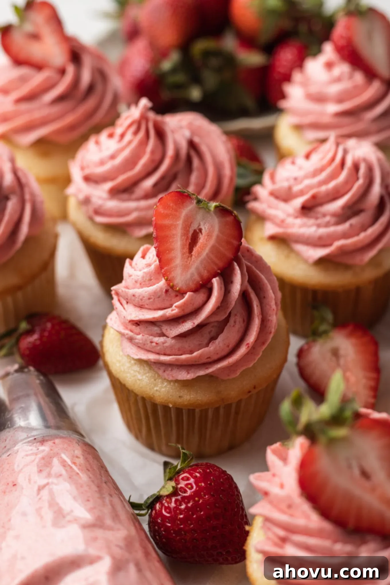 A delightful arrangement of vanilla cupcakes lavishly topped with fluffy pink strawberry frosting. A piping bag with additional frosting sits nearby, hinting at more delicious creations.