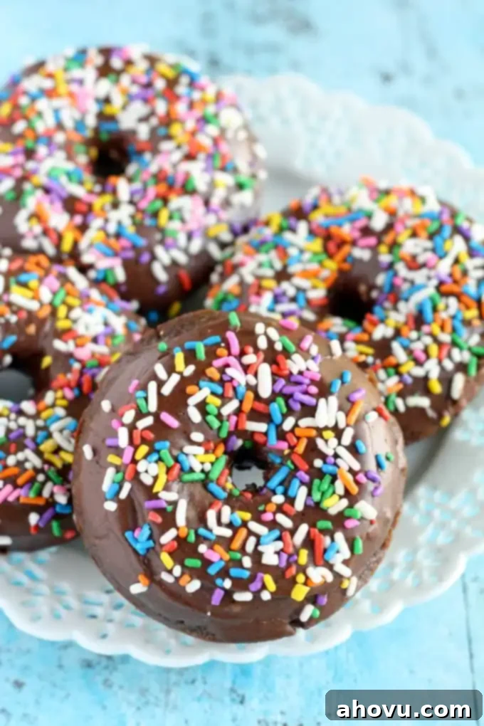 Four chocolate frosted donuts on a white dessert plate. Each donut is coated in sprinkles. 