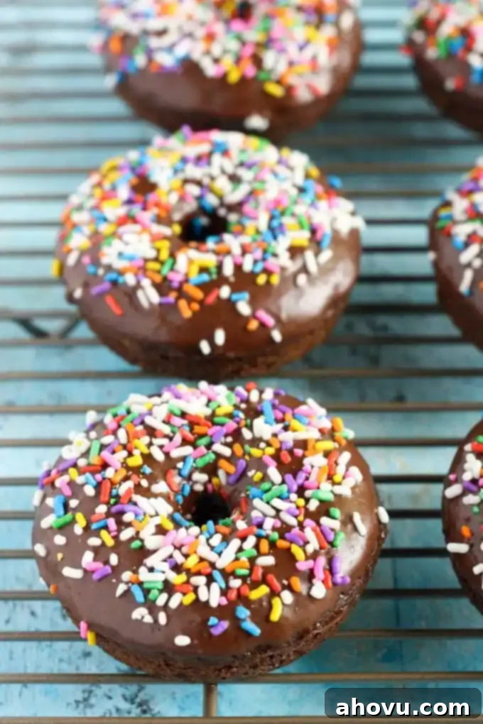 Baked chocolate frosted donuts on a wire cooling rack. Each donut is topped with sprinkles. 