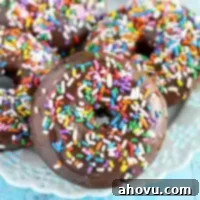 Four baked chocolate donuts topped with chocolate glaze and sprinkles on a white plate.