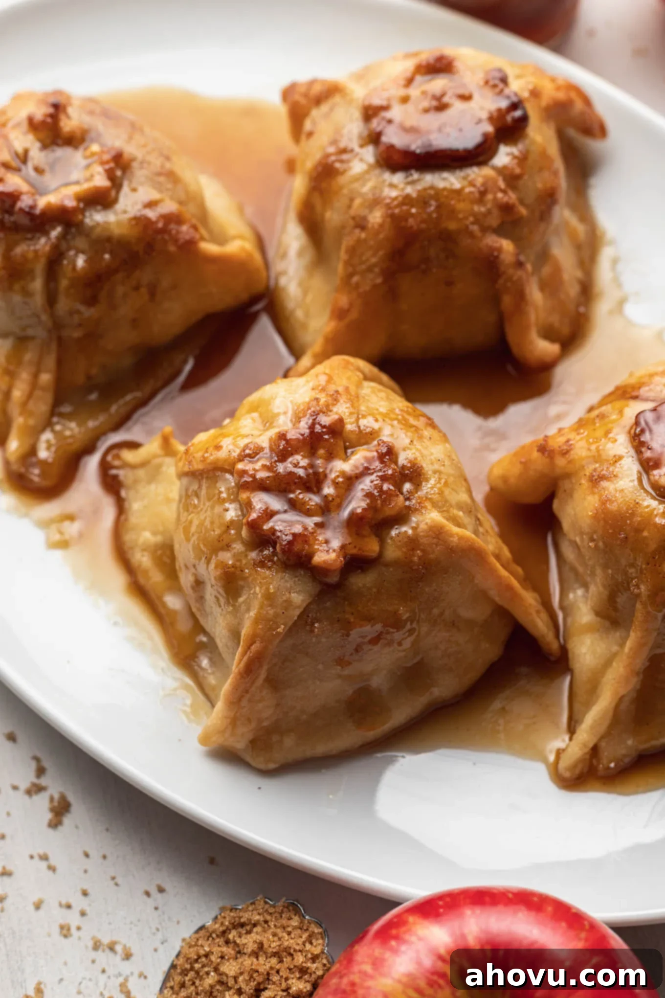 Four homemade apple dumplings with sauce on a white platter. 