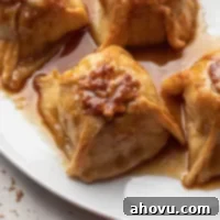 Four baked apple dumplings on a large white plate. The dumplings have been drizzled with extra sauce from the pan.