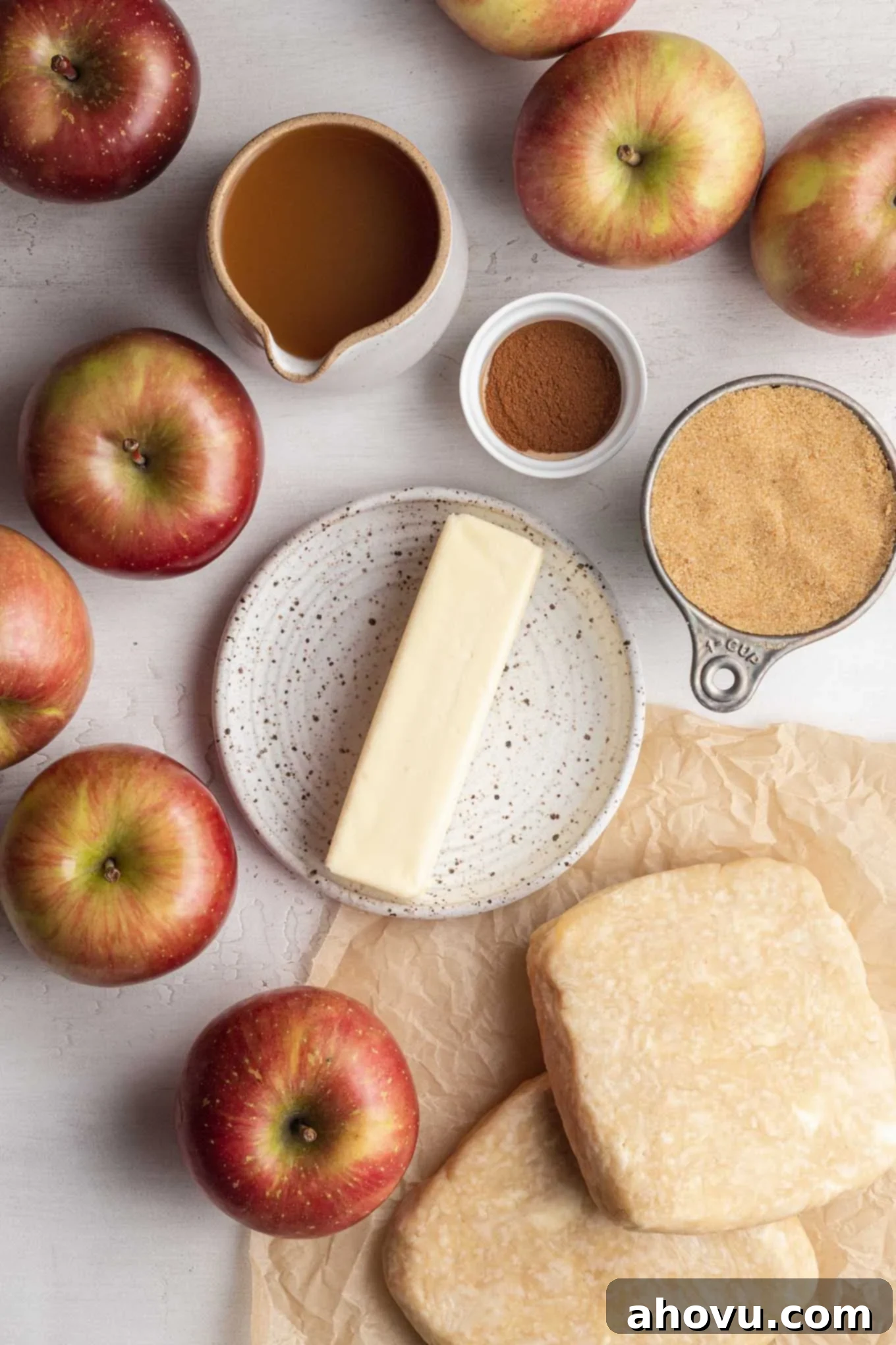 An overhead view of apples, apple cider, brown sugar, cinnamon, butter, and pie crust.