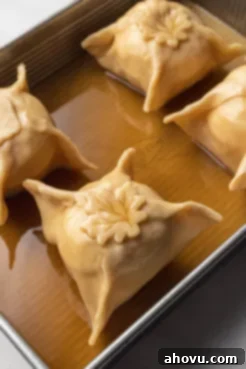 Unbaked apple dumplings with sauce in a baking tray.
