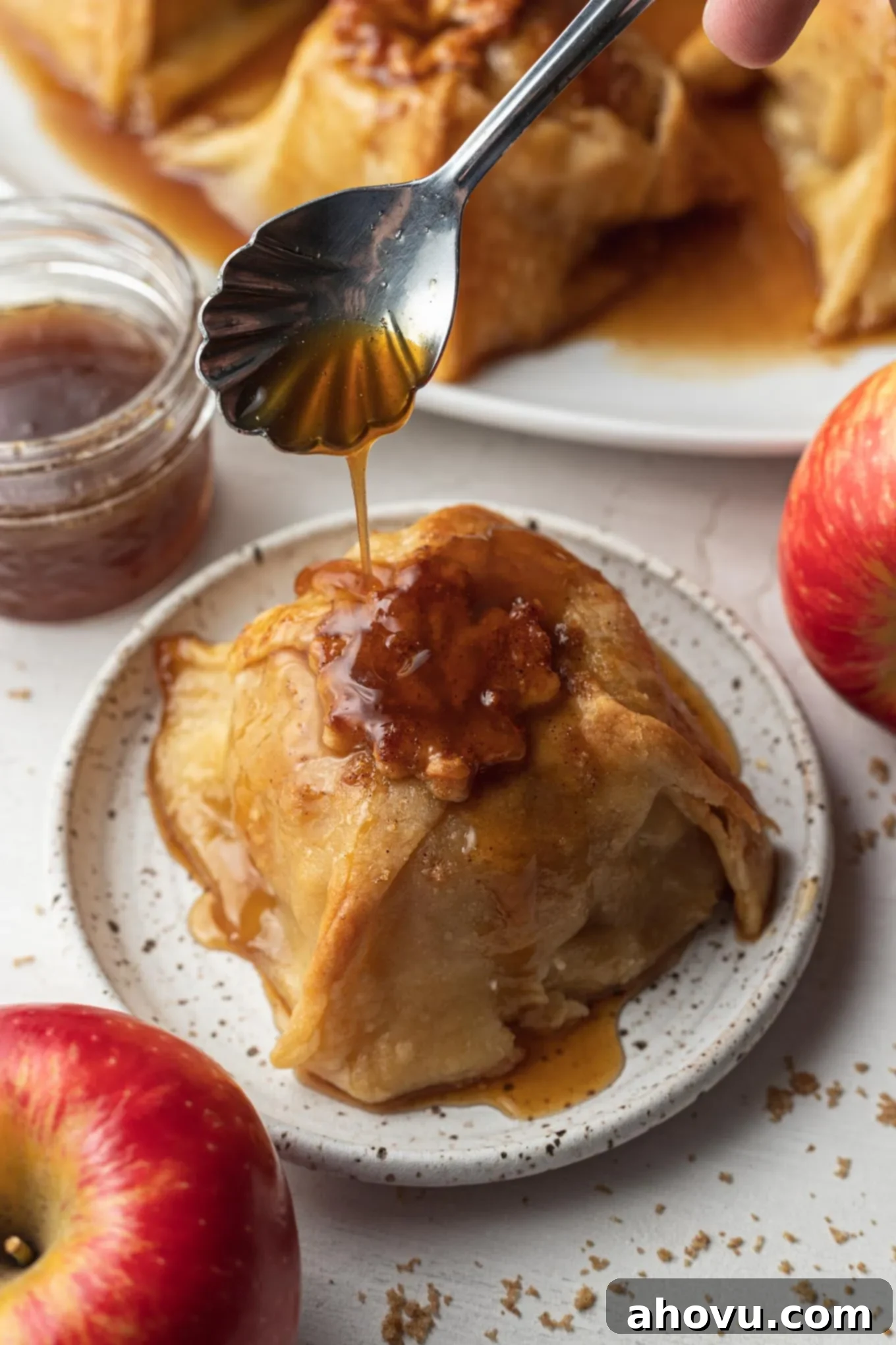 Sauce being spooned over a baked apple dumpling on a dessert plate. 