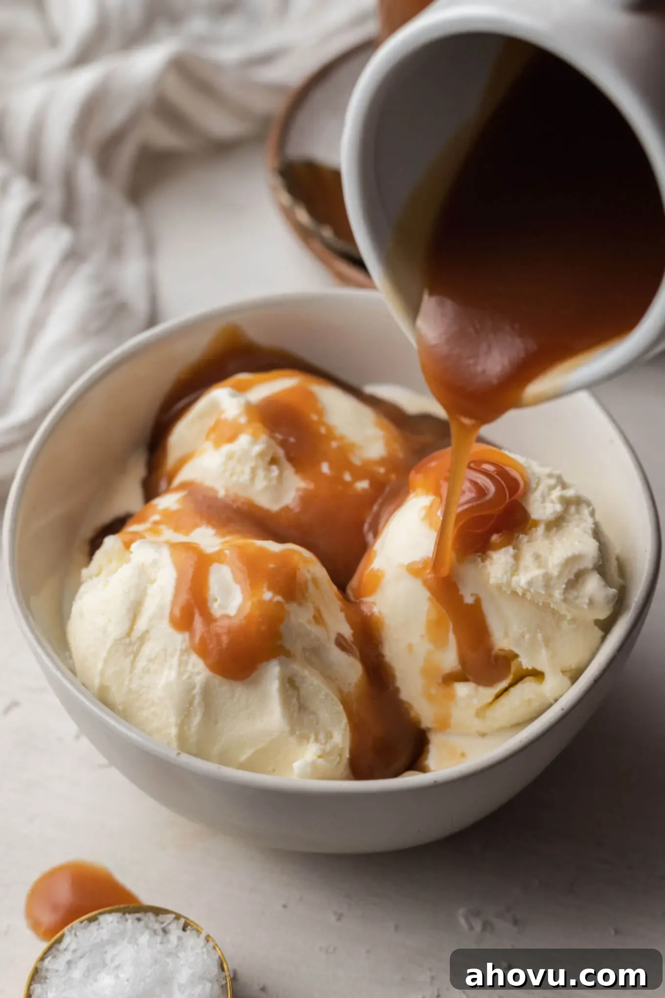 Salted caramel sauce being drizzled over a bowl of vanilla ice cream. 