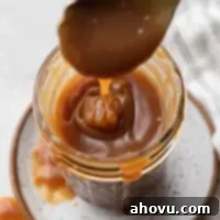 An overhead view of salted caramel sauce in a jar. A spoon is being lifted from the jar.