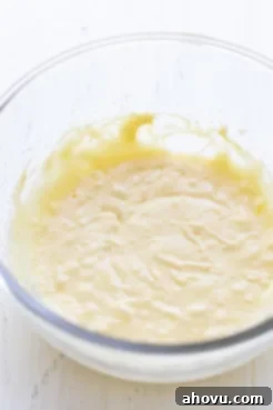 A glass mixing bowl holding the wet ingredients for the cake, including melted butter and sugar, preparing for further mixing.