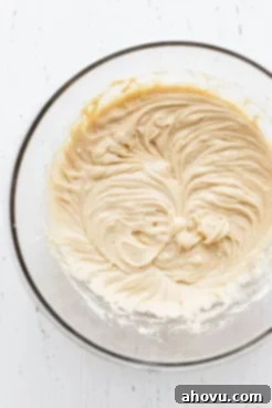 A glass mixing bowl holding the smoothly mixed finished cake batter, ready to be poured over the apples.