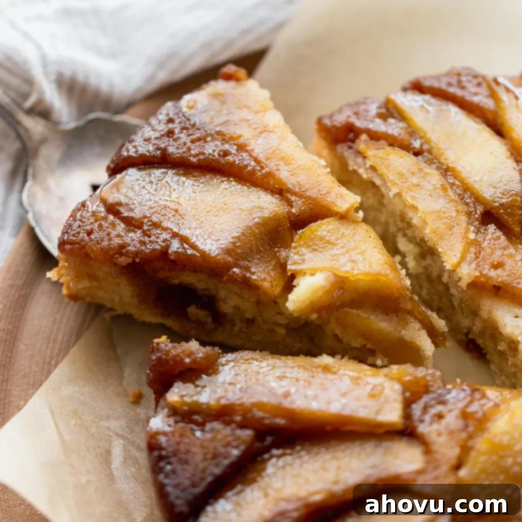 A slice of the moist apple upside-down cake being lifted from the whole cake, revealing its soft, fluffy texture and delicious caramelized apple layer.