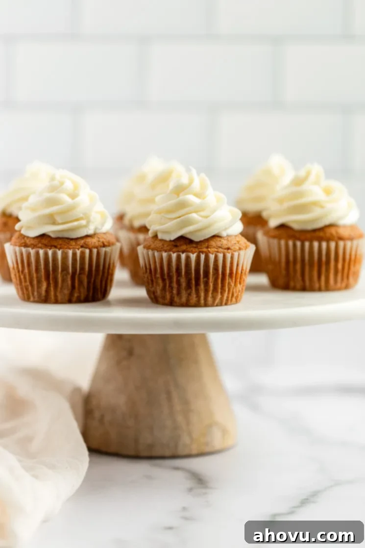 A group of perfectly baked pumpkin cupcakes, generously topped with swirls of homemade cream cheese frosting, elegantly arranged on a rustic marble cake stand.