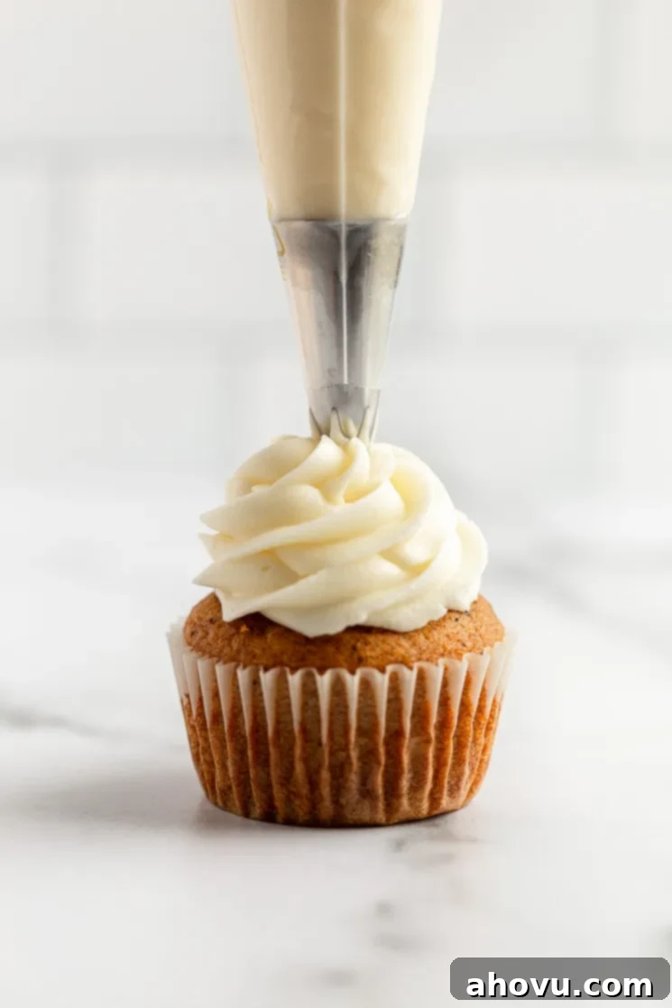 A single, unfrosted pumpkin cupcake being meticulously topped with creamy, white cream cheese frosting using a piping bag with a star tip.