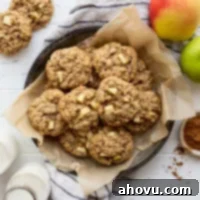 An overhead image of perfectly baked apple oatmeal cookies arranged in a metal baking dish, surrounded by fresh apples and cinnamon sticks, highlighting their warm, inviting appeal.