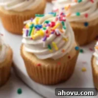 Vanilla cupcakes topped with sprinkles on a around marble serving platter.