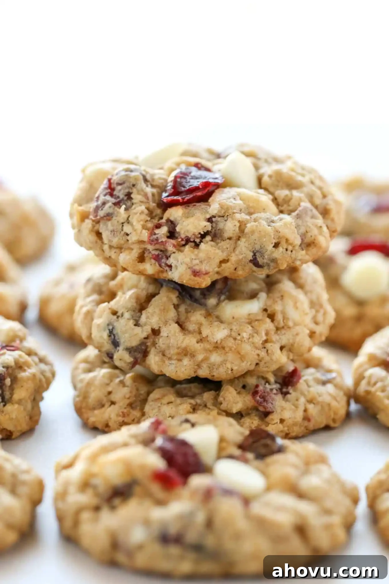 A beautiful stack of three soft and chewy white chocolate cranberry oatmeal cookies. More delicious cookies are arranged artfully around the stack, ready for serving.