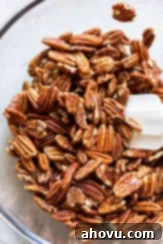 Pecan halves being gently mixed in a glass bowl with the frothy egg white mixture, ensuring an even coating on each nut.