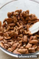 A glass bowl filled with pecan halves, now thoroughly coated in the fragrant cinnamon sugar mixture, glistening and ready for baking.