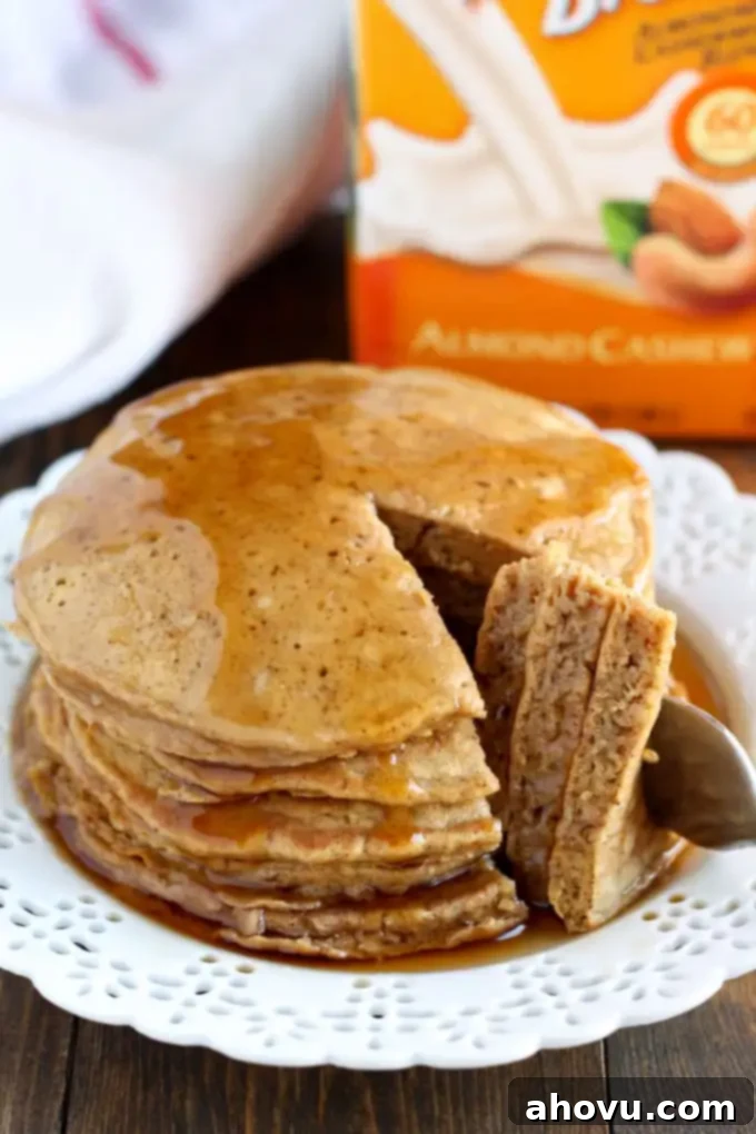 Cozy Gingerbread Flapjacks 2 A beautifully stacked tower of golden-brown gingerbread pancakes on a white plate, with a bite playfully taken out, revealing the fluffy interior. A sprinkle of powdered sugar dusts the top, and a pool of golden maple syrup surrounds the base.