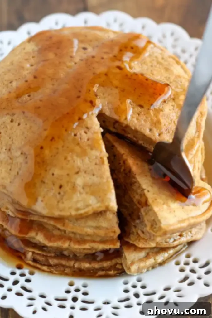 Cozy Gingerbread Flapjacks 5 A vibrant, close-up shot of a stack of gingerbread pancakes, artfully presented on a white plate. A perfect bite has been removed, showcasing the tender, fluffy interior. The pancakes are glistening with golden maple syrup, ready to be enjoyed.