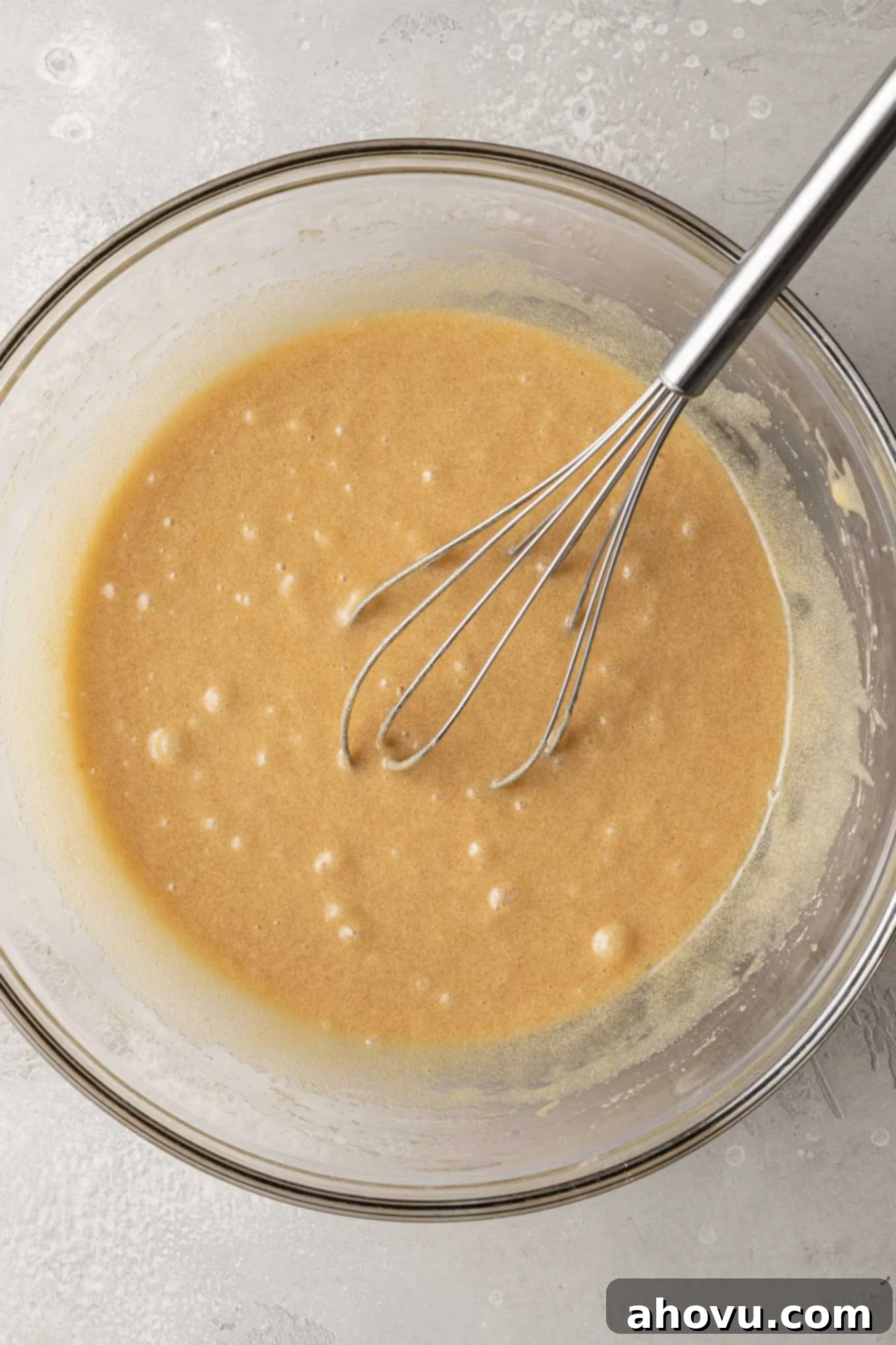 An overhead view of the wet ingredients for snickerdoodle blondies, including melted butter, sugars, eggs, and vanilla, in a clear glass mixing bowl, ready to be whisked.