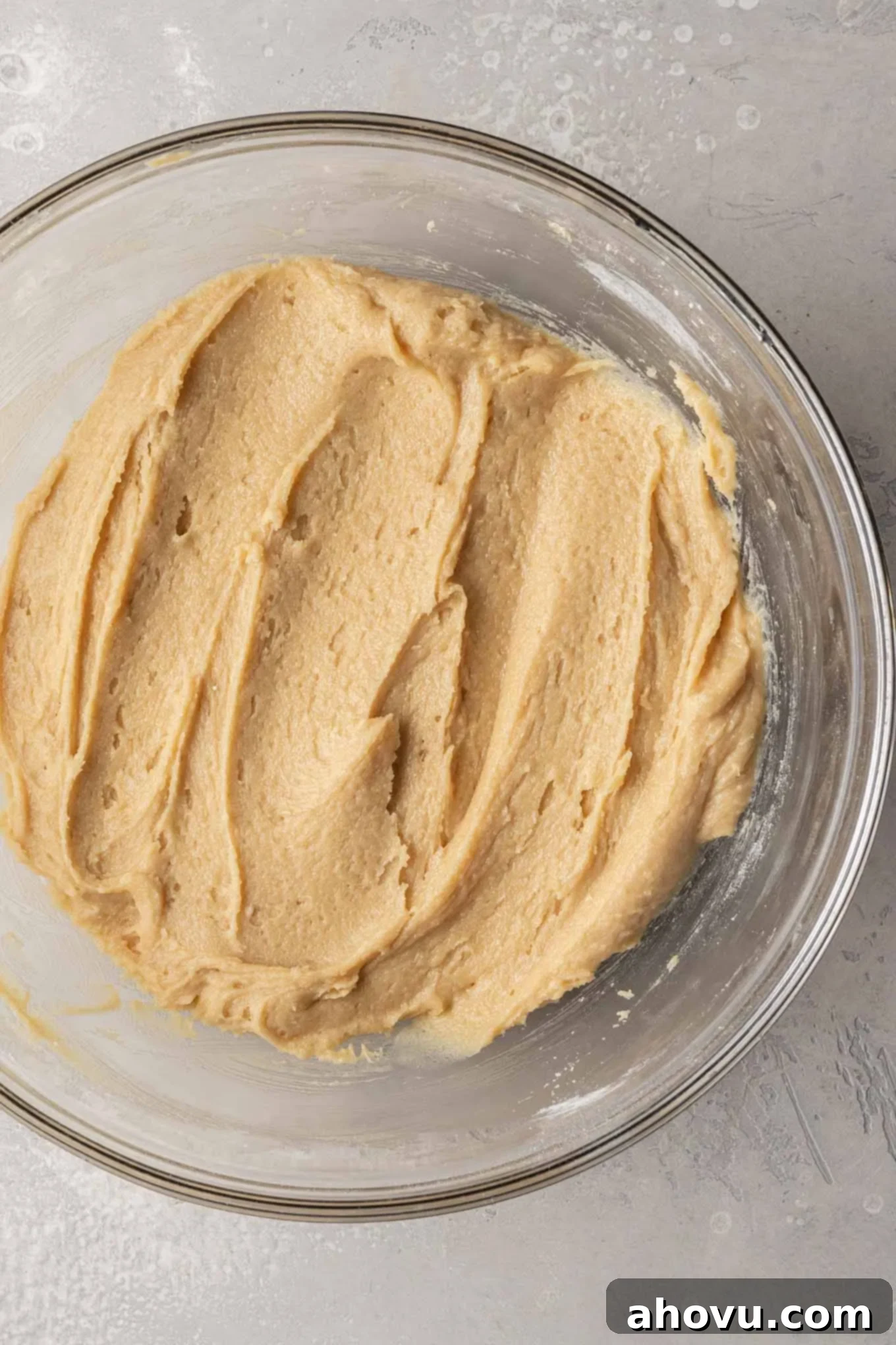An overhead view of snickerdoodle cookie dough in a glass mixing bowl after wet and dry ingredients have been combined, showing its rich, golden-brown color and thick texture.