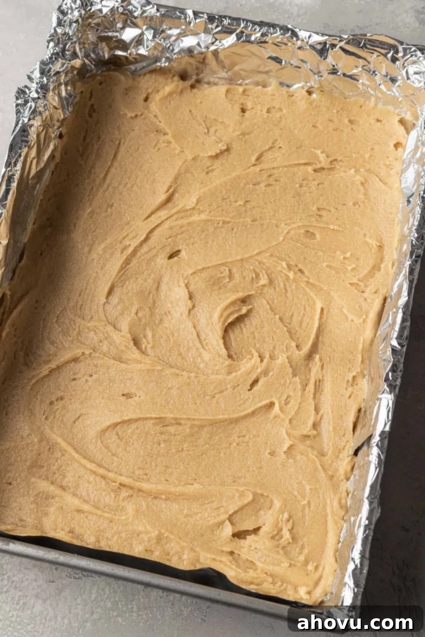Smooth snickerdoodle cookie dough spread evenly in a 9x13 pan lined with foil, ready for the cinnamon-sugar topping.