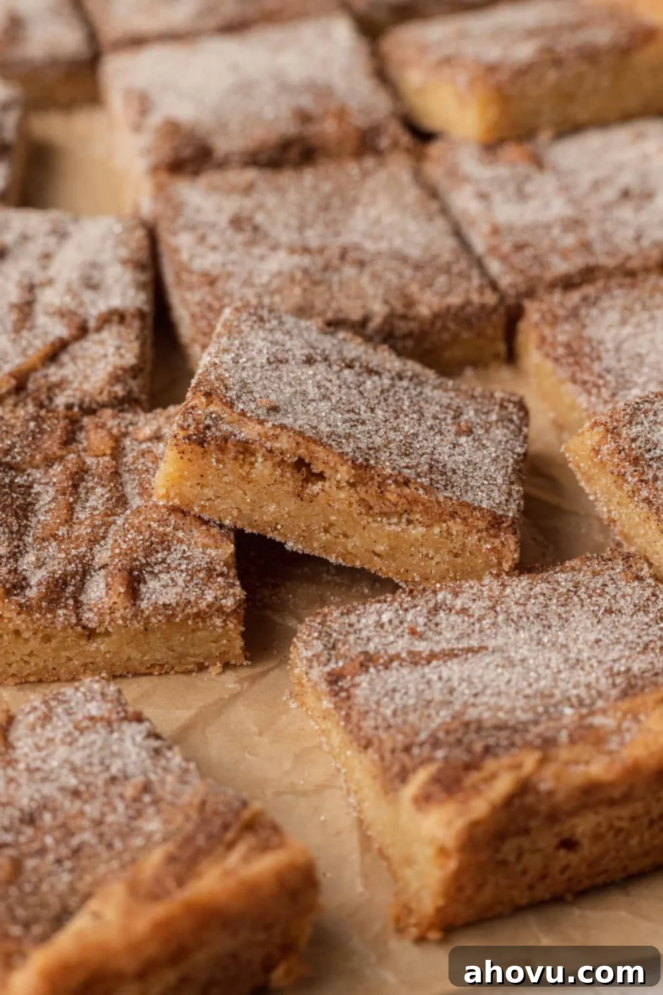A side view of perfectly sliced snickerdoodle blondies arranged on parchment paper. One cookie bar is propped up in the middle, highlighting its soft, chewy texture.