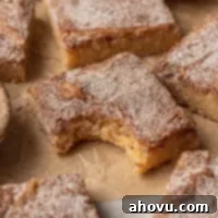 A snickerdoodle blondie with a bite taken out on a brown piece of parchment paper. More blondies are scattered around it.