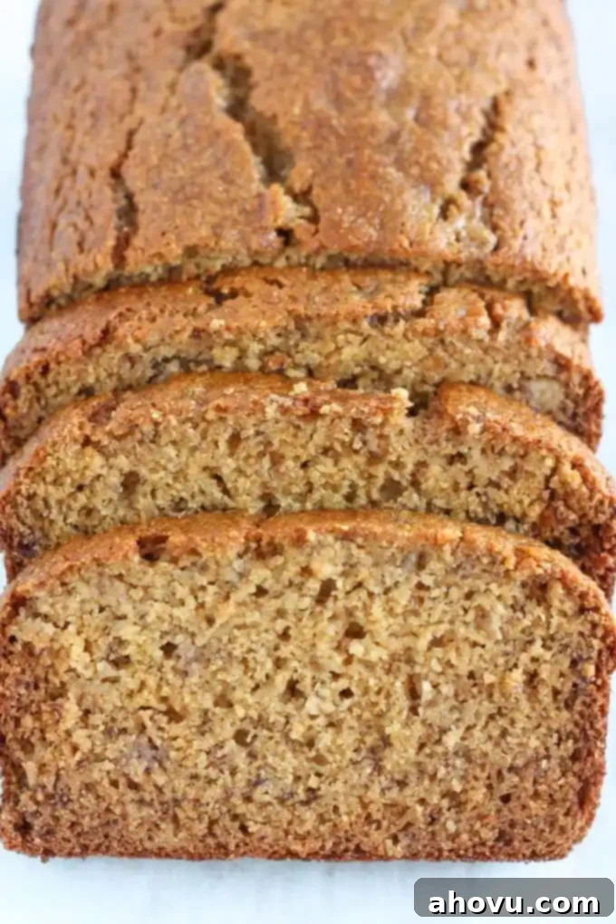 A perfectly baked loaf of healthy whole wheat banana bread on a wooden board, with three slices cut from the front, revealing its moist, golden interior and bits of banana.