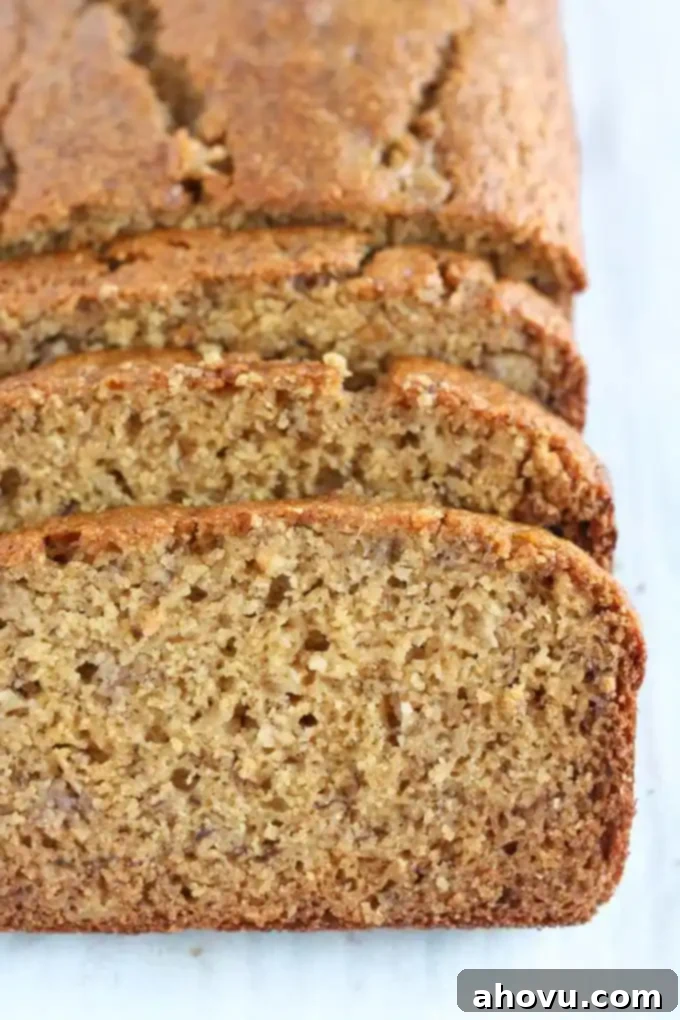 A whole wheat banana bread loaf, freshly baked and still in the pan, with the front section neatly sliced into serving portions, showcasing its inviting texture.