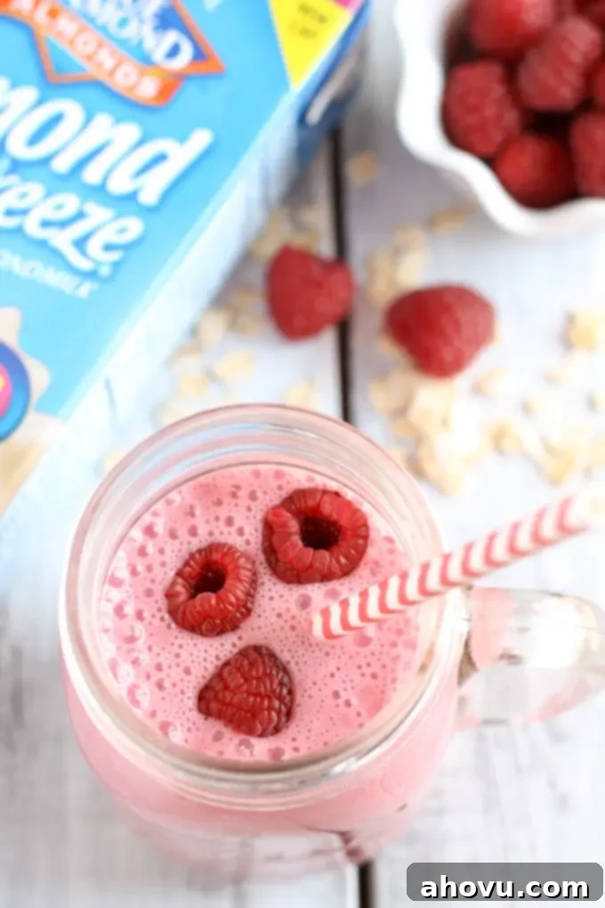 Overhead view of a raspberry almond milk smoothie next to a carton of almond milk and a bowl of fresh berries. 