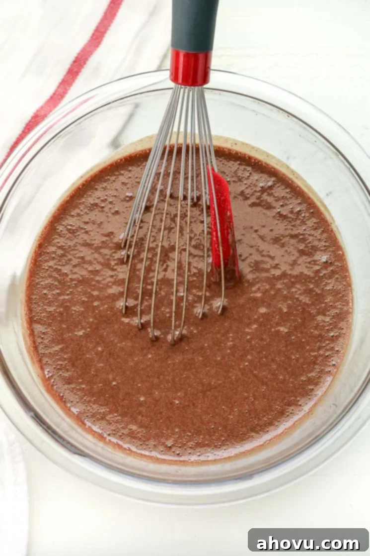 A clear bowl filled with chocolate cupcake batter and a whisk.