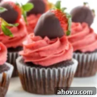 A closeup of chocolate cupcakes topped with strawberry buttercream frosting and chocolate covered strawberries.