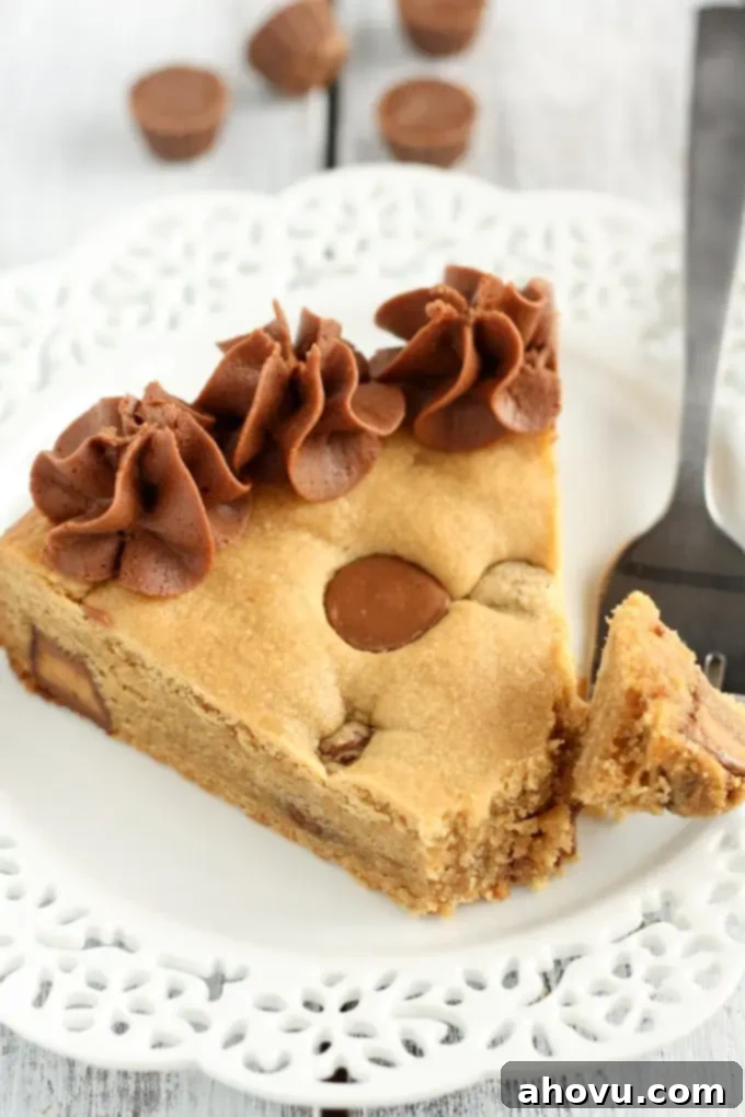 Giant Peanut Butter Cup Cookie 2 A perfectly baked slice of homemade peanut butter cup cookie cake on a pristine white plate, accompanied by a fork, ready to be enjoyed.