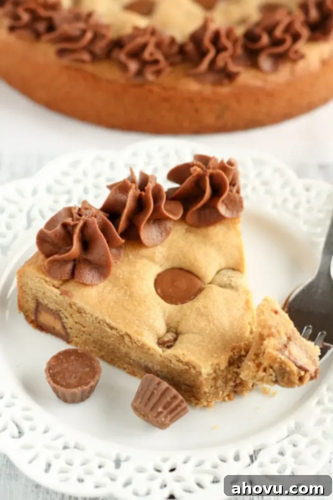 Giant Peanut Butter Cup Cookie 4 A delectable slice of homemade peanut butter cup cookie cake, served on a white plate with a fork, with the remainder of the giant cookie cake subtly blurred in the background.