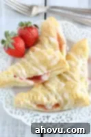 A freshly baked strawberry turnover, with a delicate glaze drizzle, placed next to a few whole strawberries and a small white bowl. This shows the finished product, ready to be enjoyed.