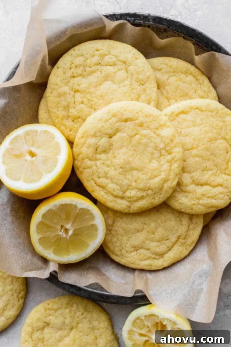 A round pan holding baked lemon cookies with a lemon cut in half beside them, showcasing their soft, golden texture and fresh appeal.