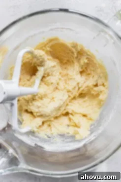 A glass mixing bowl holding creamy cookie batter with a beater still in it, illustrating the mixing process for lemon cookies.