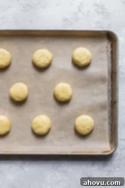 A cookie sheet lined with parchment paper holding neatly scooped balls of lemon cookie dough, ready for baking.